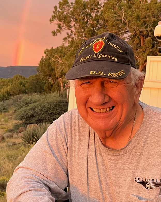 photo of David Devaney sitting outside with a rainbow in the background