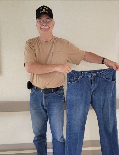 Photo of a John Smith, after losing weight with MOVE, standing while holding a large pair of pants he used to wear.