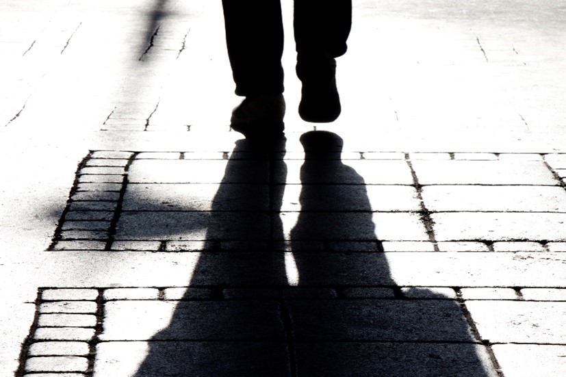 Photo of person's feet and legs in silhouette shadow walking away on cobblestone street in black and white