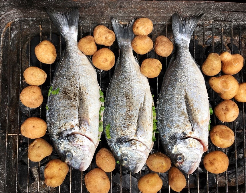 Photo of directly above shot of fish and potatoes on a barbecue grill