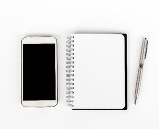 Photo of a mobile phone and white blank spiral notebook with pen
